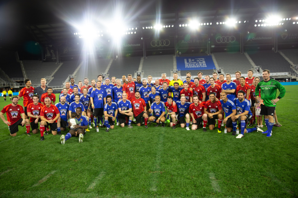 Members of congress and athletes on both red and blue teams pose together for a group photo under the lights at Audi Field